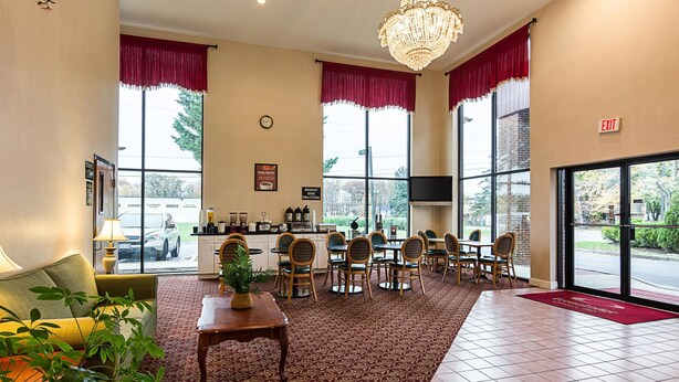 A hotel lobby with a dining area, large windows, a chandelier, and a clock on the wall. - Econo Lodge Andrews Air Force Base (Clinton)