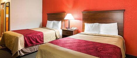 A hotel room with two beds, each with a wooden headboard, a nightstand with a lamp, and a red accent wall.