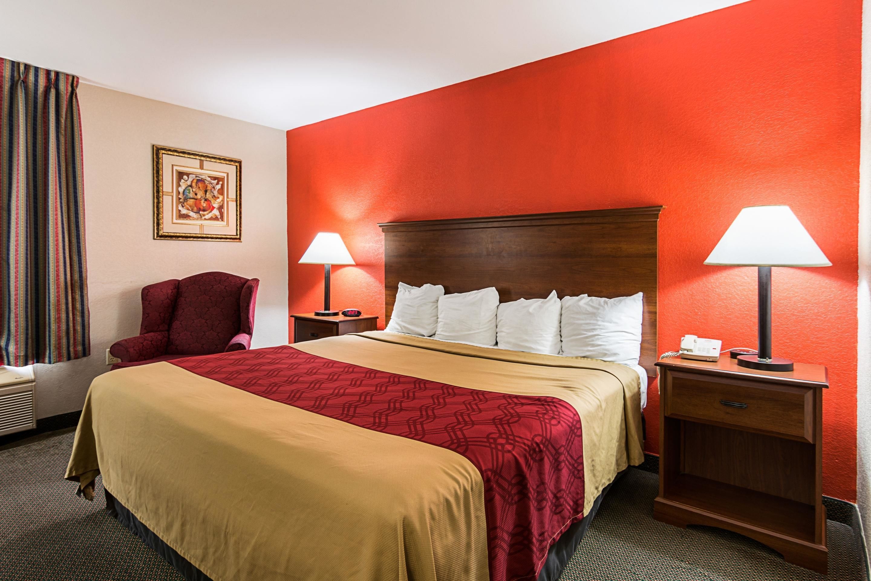 A hotel room with a large bed, two bedside tables, a chair, and a red accent wall.