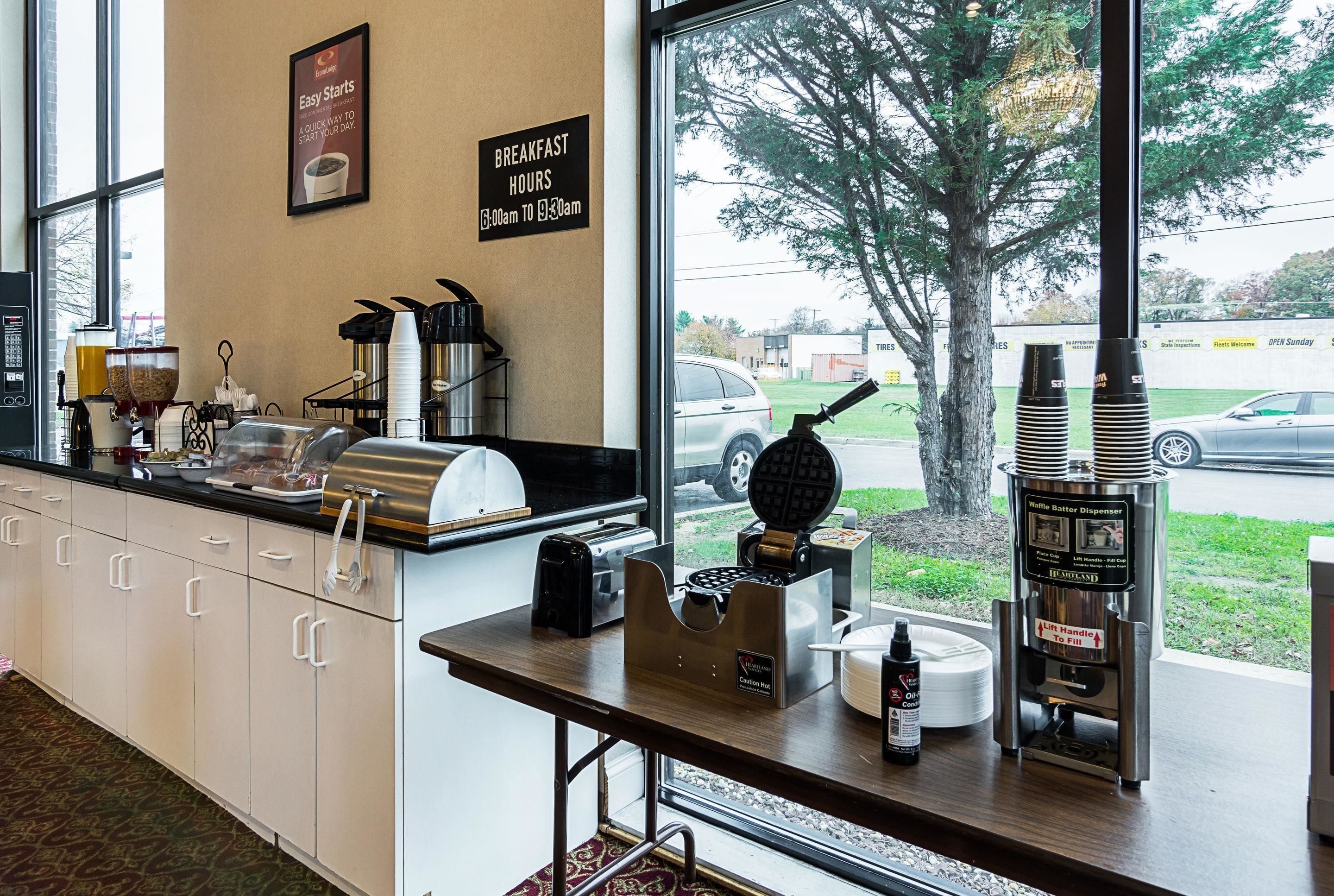 A breakfast bar with a waffle maker, coffee machine, and a sign indicating breakfast hours.