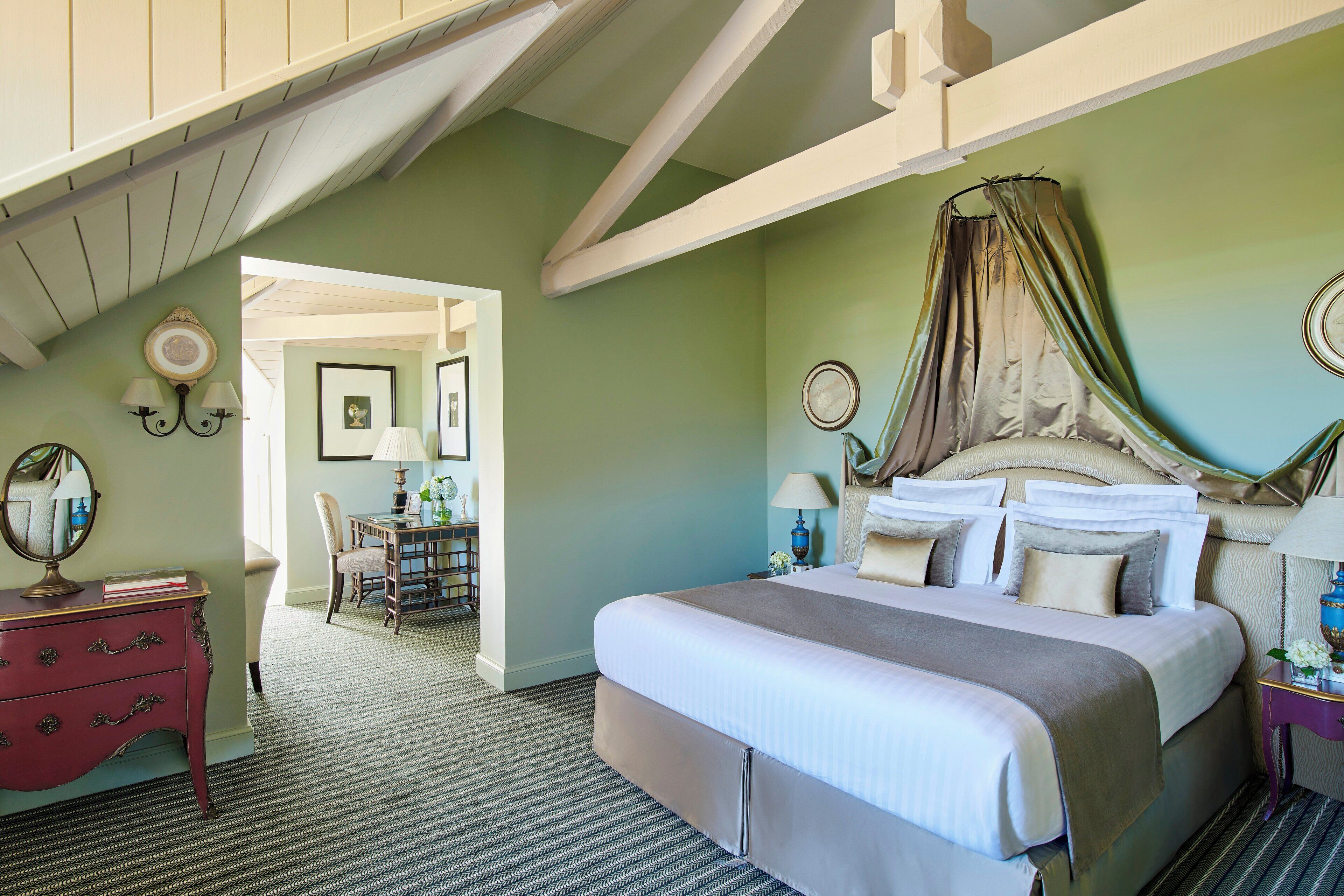 A bedroom with a large bed, a vanity with a mirror, and a desk with a chair.