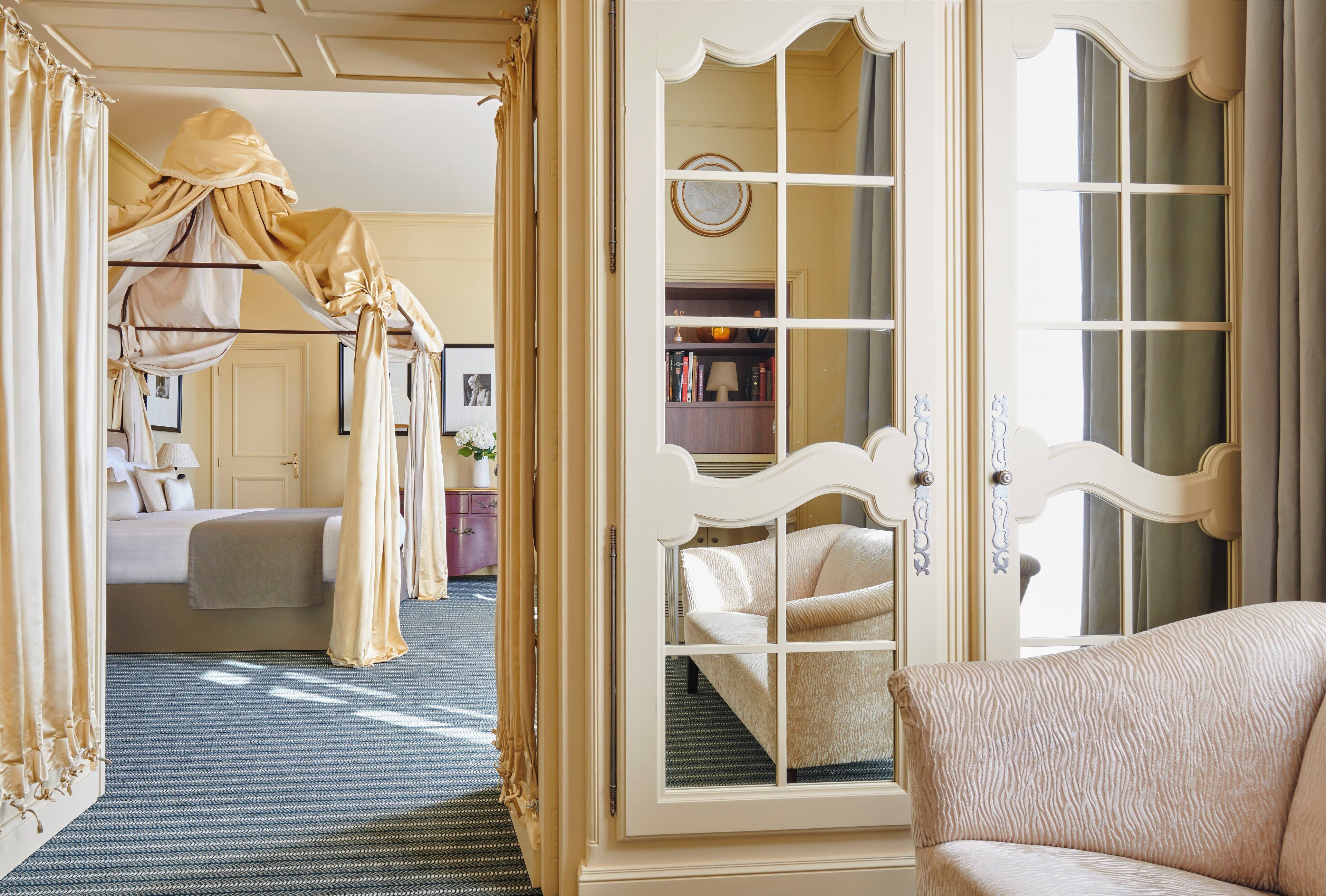 A bedroom with a canopy bed, a sitting area with a chair, and a view through a window.