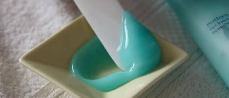 Una mano sostiene un objeto blanco sobre un pequeño recipiente con una sustancia azul verdosa.