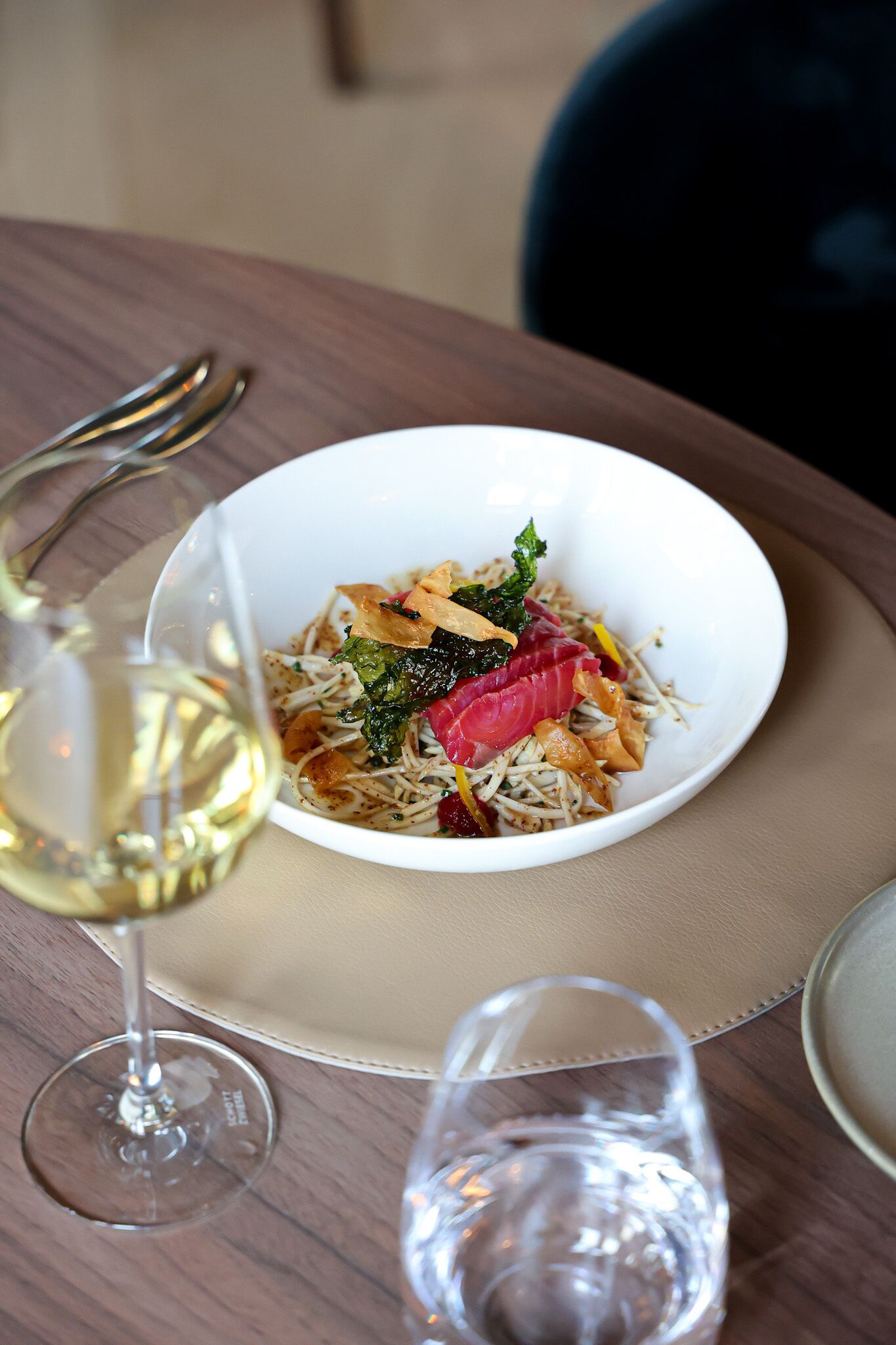 A white bowl of food on a table with a wine glass and a water glass.