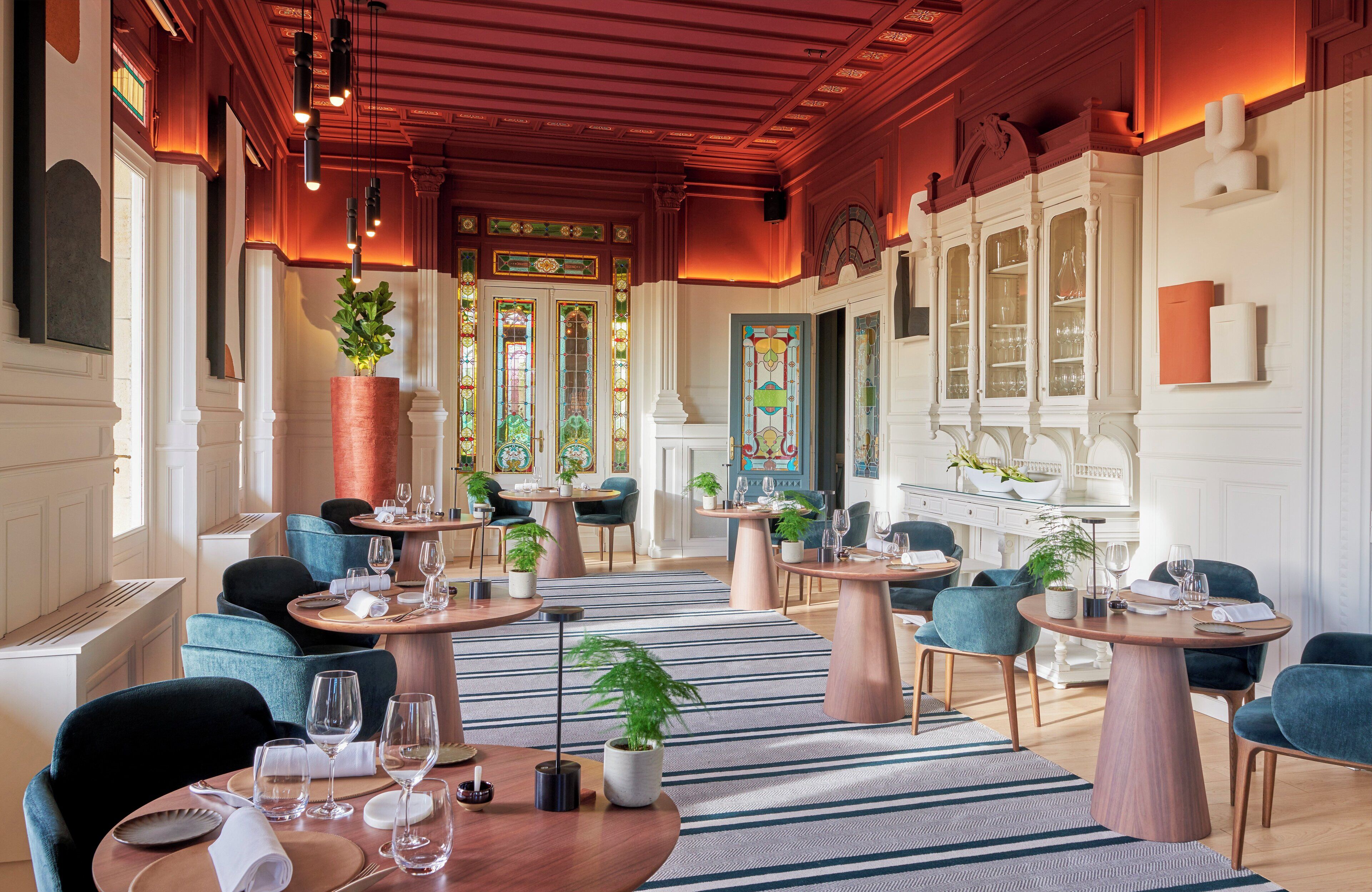 Un restaurant avec des tables rondes, des chaises bleues et des plantes en pot.