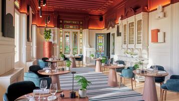 A restaurant with round tables, blue chairs, and potted plants.