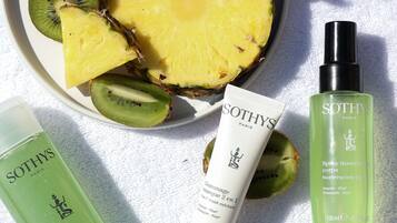 Un plato con rodajas de piña y kiwi, dos productos para el cuidado de la piel y una botella con pulverizador.