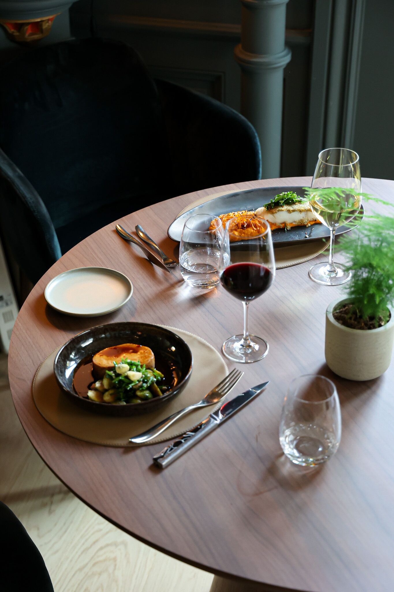 A dining table with plates of food, wine glasses, and cutlery.