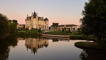 A large, historic building with a symmetrical facade, a central dome, and a reflection in a calm body of water.