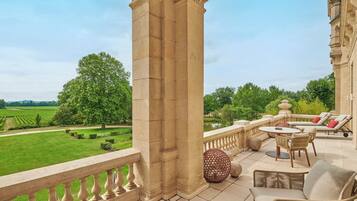 A balcony with a stone balustrade, wicker furniture, and a view of a green landscape.