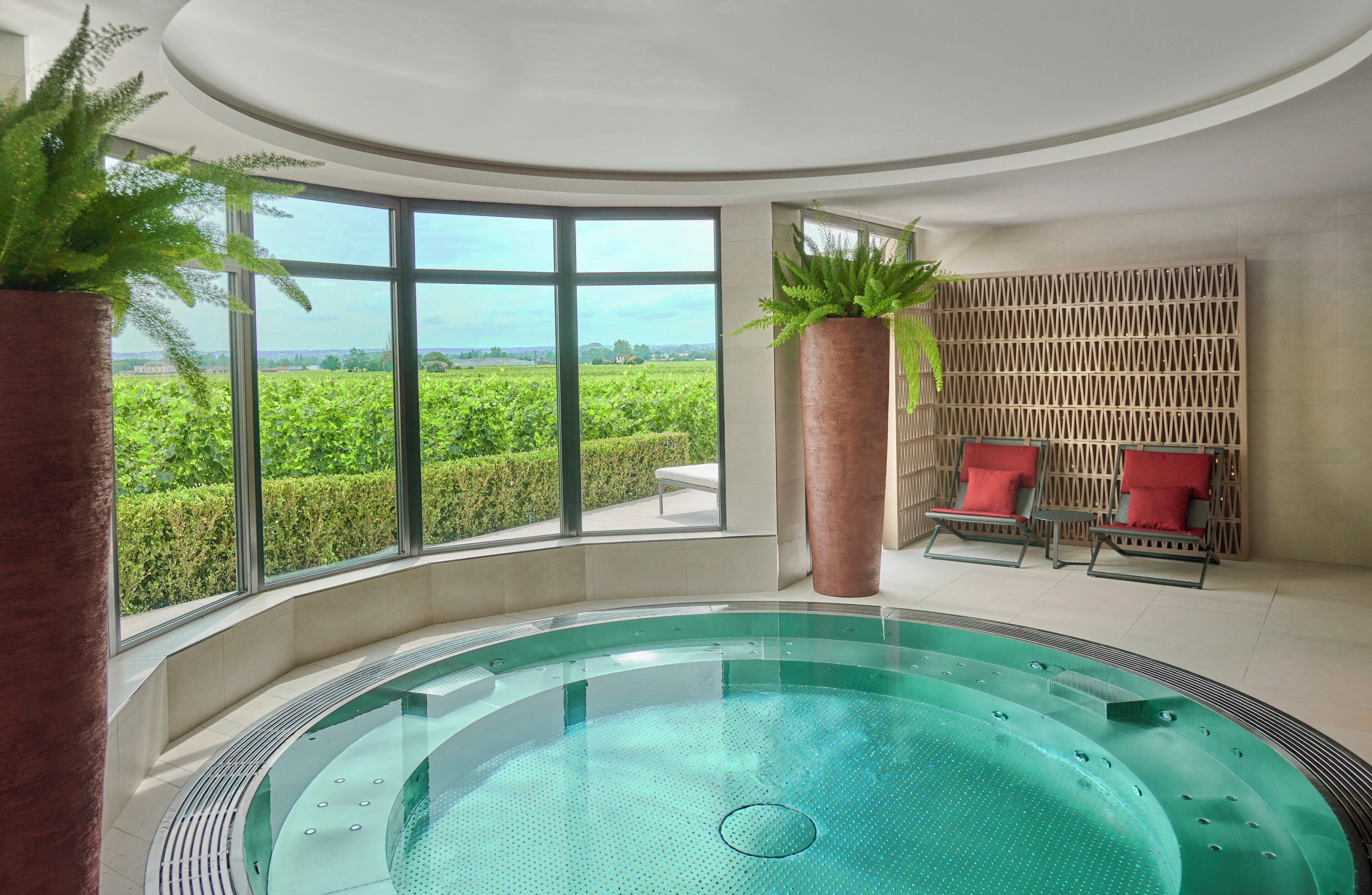 A spa area with a hot tub, large windows, and red chairs.