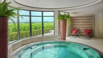 A spa area with a hot tub, large windows, and red chairs.