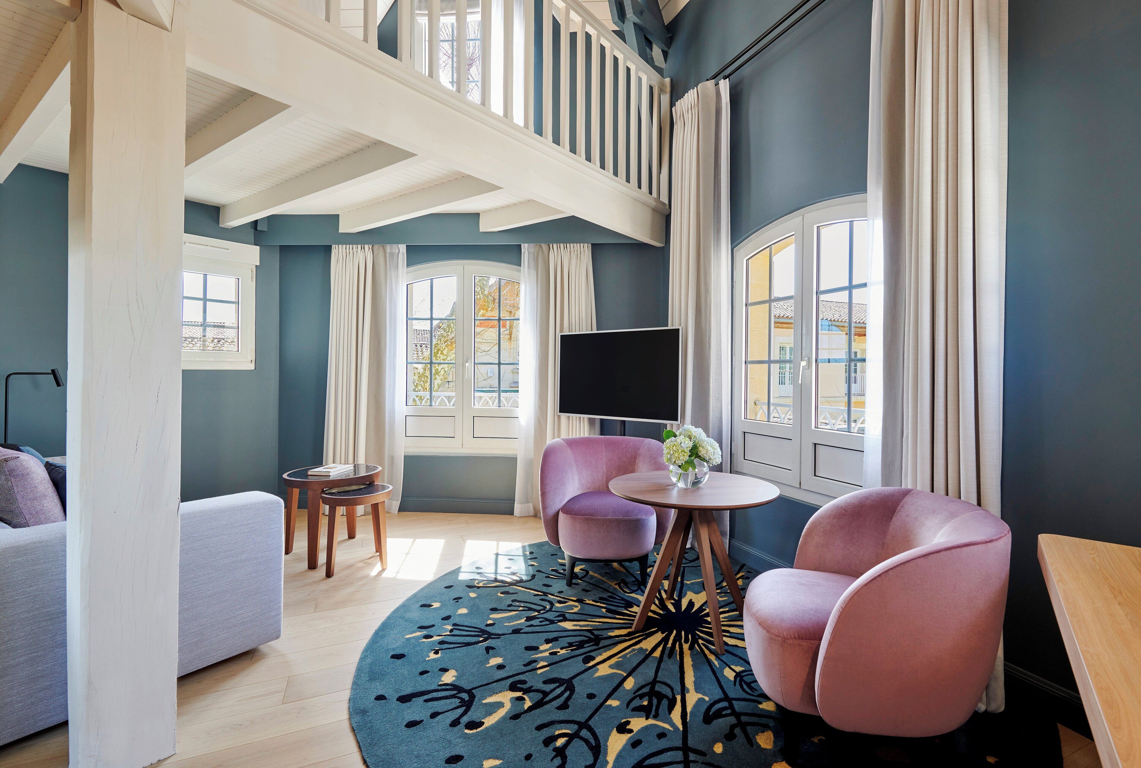 A modern living room with a high ceiling, a large window, a flat-screen TV, a round coffee table, and a sofa.