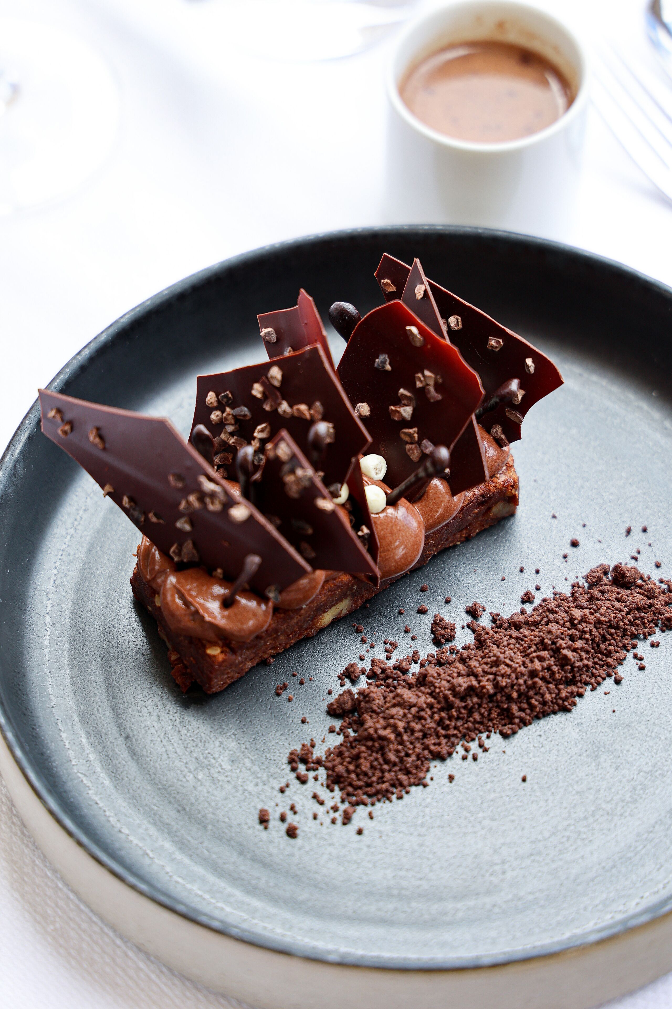 A dessert on a plate with a cup of coffee in the background.