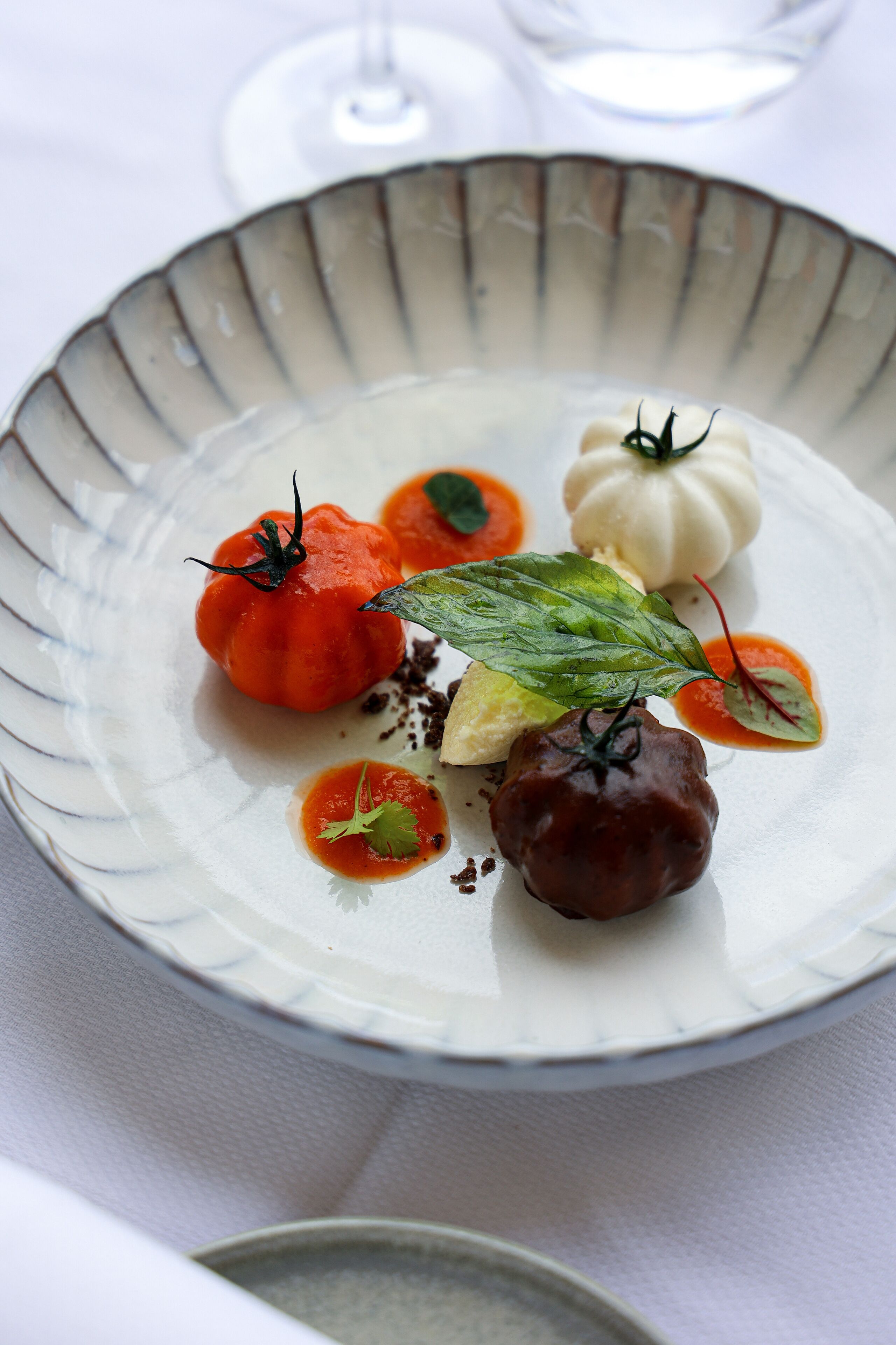 A plate with various food items, including a tomato, a leaf, and a dollop of sauce.