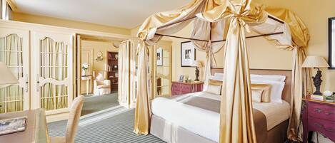 A room with a four-poster bed, a desk with a chair, and a vanity with a mirror.