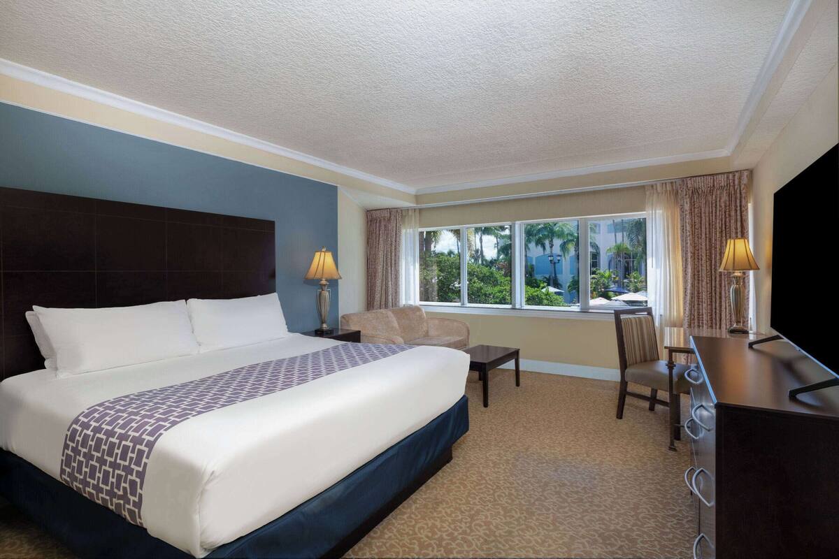A hotel room with a large bed, a desk with a chair, a TV, and a window with curtains.