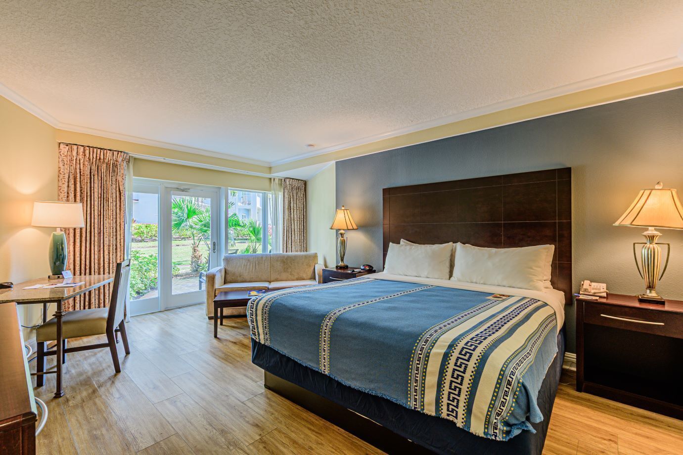 A hotel room with a large bed, a desk, a chair, a nightstand, and a lamp.