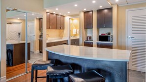 A modern kitchen with a curved island, bar stools, and built-in cabinets. - Safety Harbor Resort & Spa Trademark Collection by Wyndham (Safety Harbor)