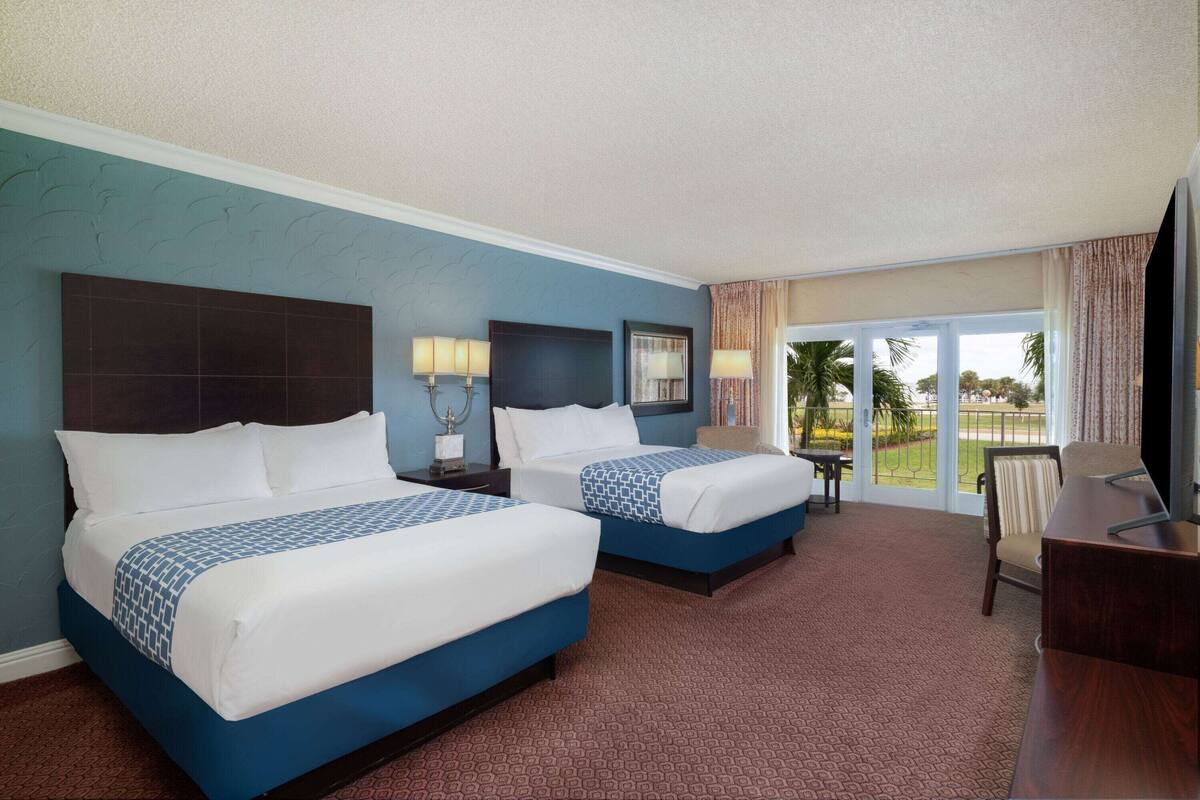 A hotel room with two beds, a desk, and a view of the outdoors.