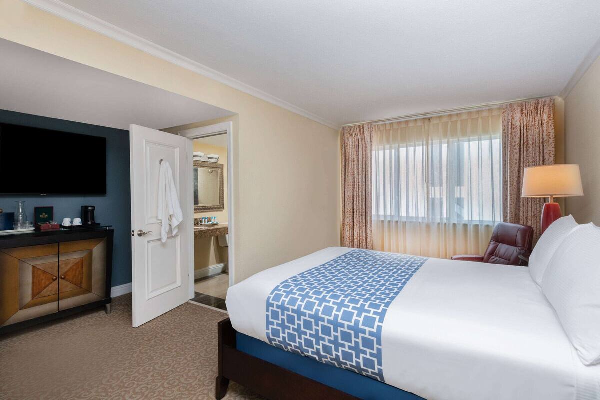 A hotel room with a bed, a TV, a desk, and a bathroom visible through an open door.