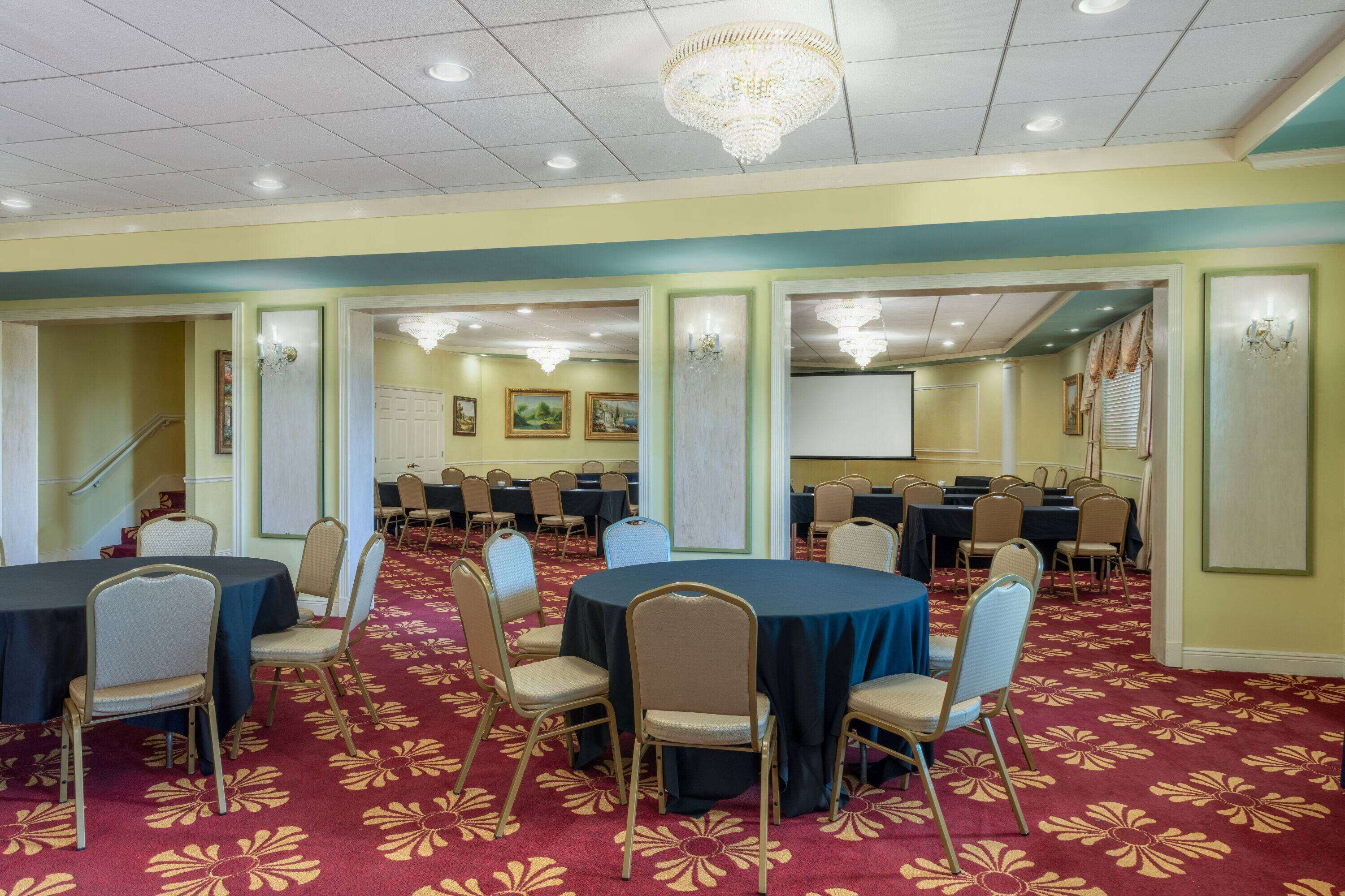 A conference room with round tables and chairs, carpeted floor, chandeliers, and framed pictures on the walls.