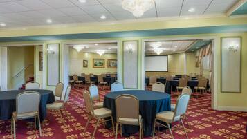 A conference room with round tables and chairs, carpeted floor, chandeliers, and framed pictures on the walls.