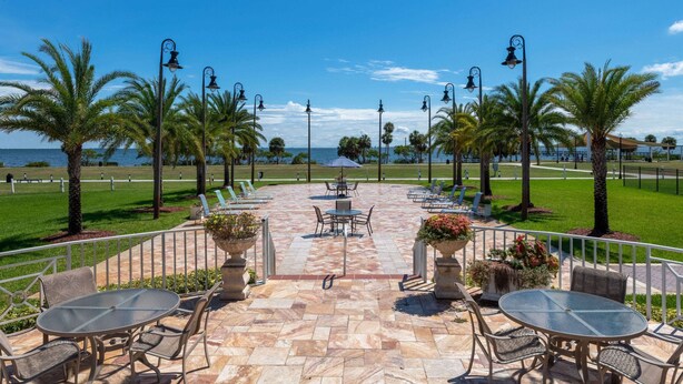 A patio with tables and chairs, palm trees, and a view of the ocean. - Safety Harbor Resort & Spa Trademark Collection by Wyndham (Safety Harbor)