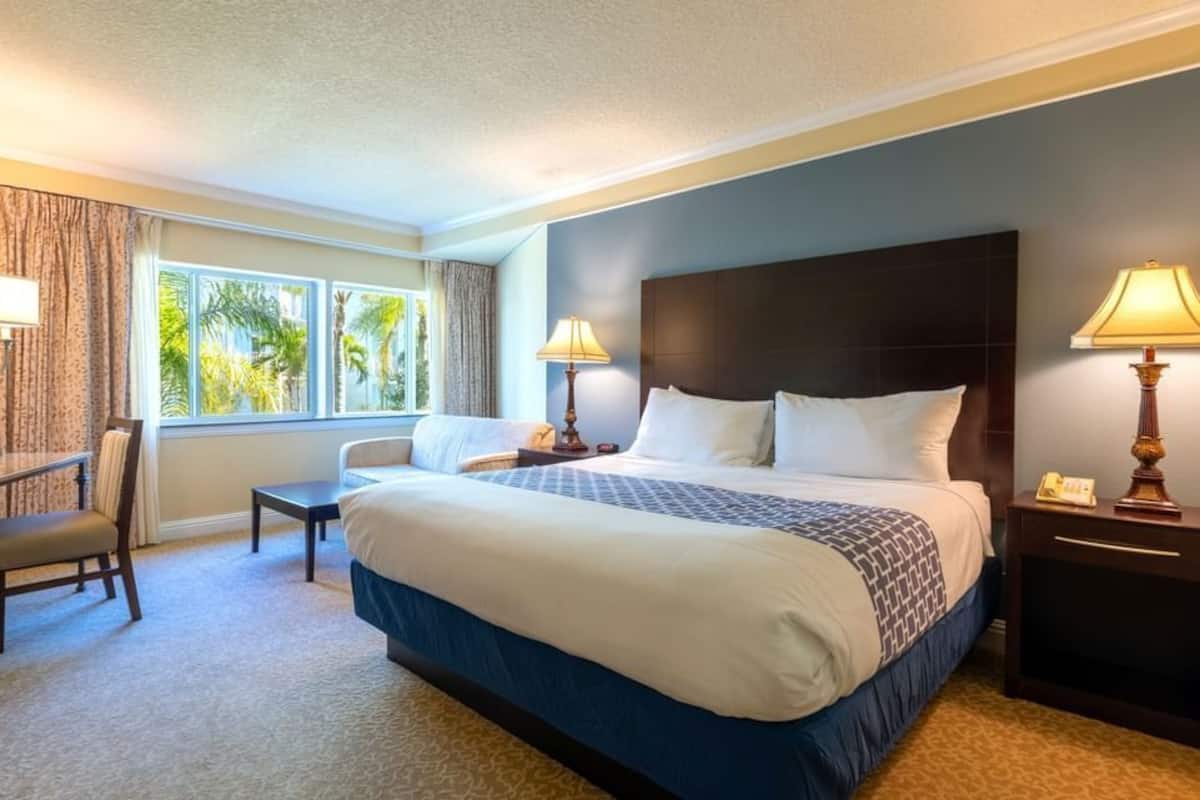 A hotel room with a large bed, two bedside tables with lamps, a desk with a chair, and a window with curtains.