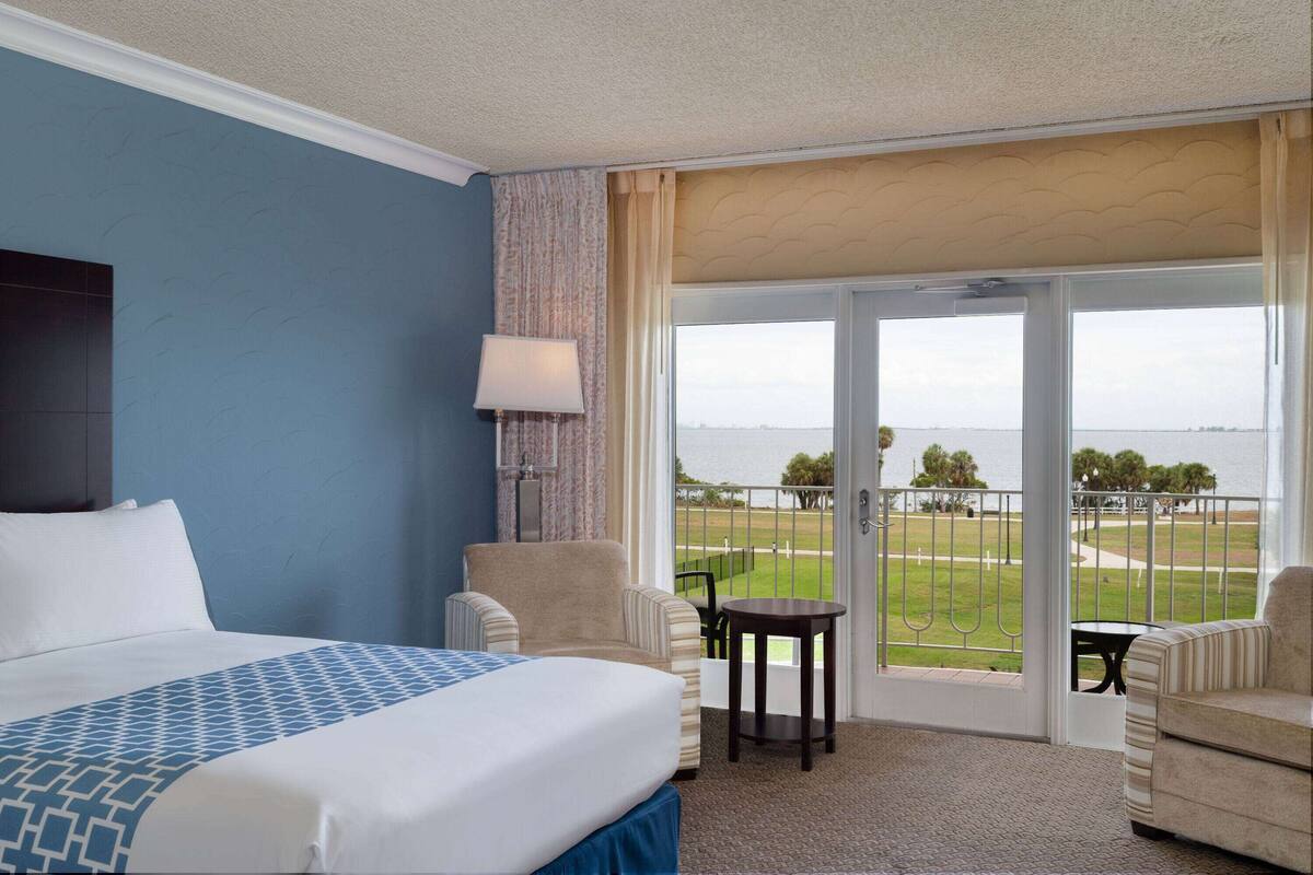 A hotel room with a large bed, two armchairs, a small table, and a balcony with a view of the sea.