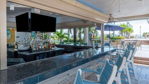 A bar area with a counter, seating, and a television screen. - Safety Harbor Resort & Spa Trademark Collection by Wyndham (Safety Harbor)