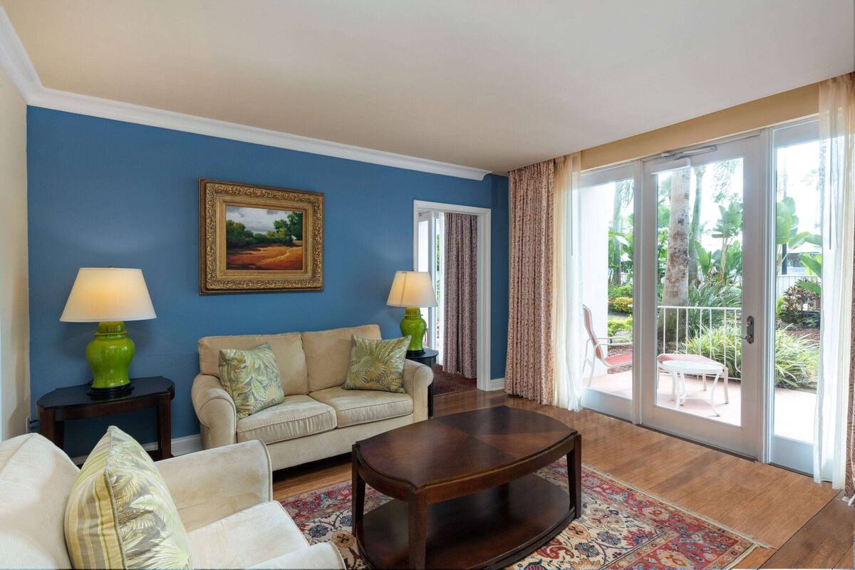 A living room with a blue wall, a beige sofa, a wooden coffee table, and a patterned rug.