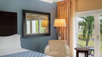 A hotel room with a bed, a chair, a table, a lamp, a mirror, and a view of the outdoors.