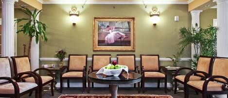 A lobby with a round table, chairs, a painting, and a vase with apples.