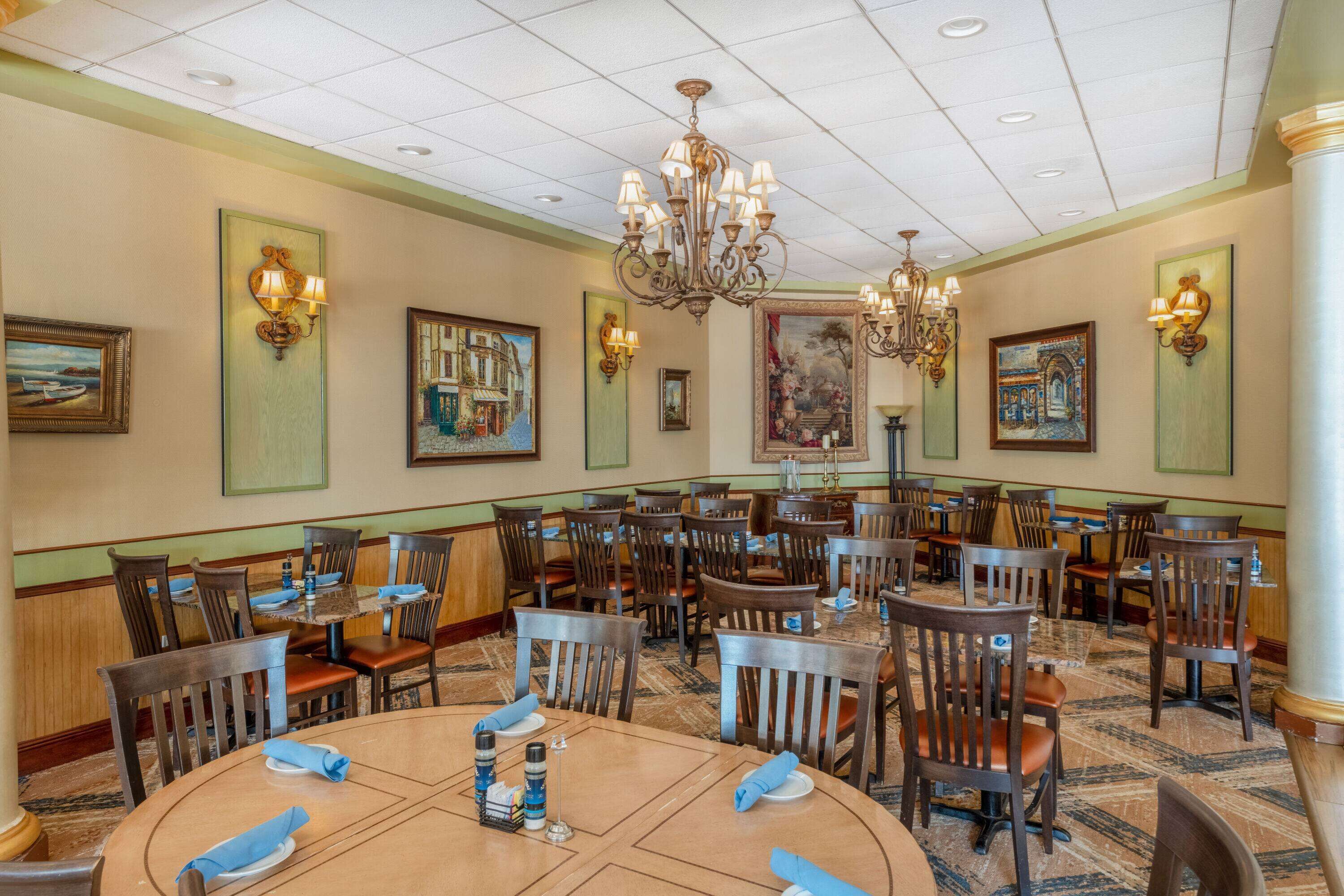 Un comedor amplio con múltiples mesas y sillas, candelabros y cuadros en las paredes.