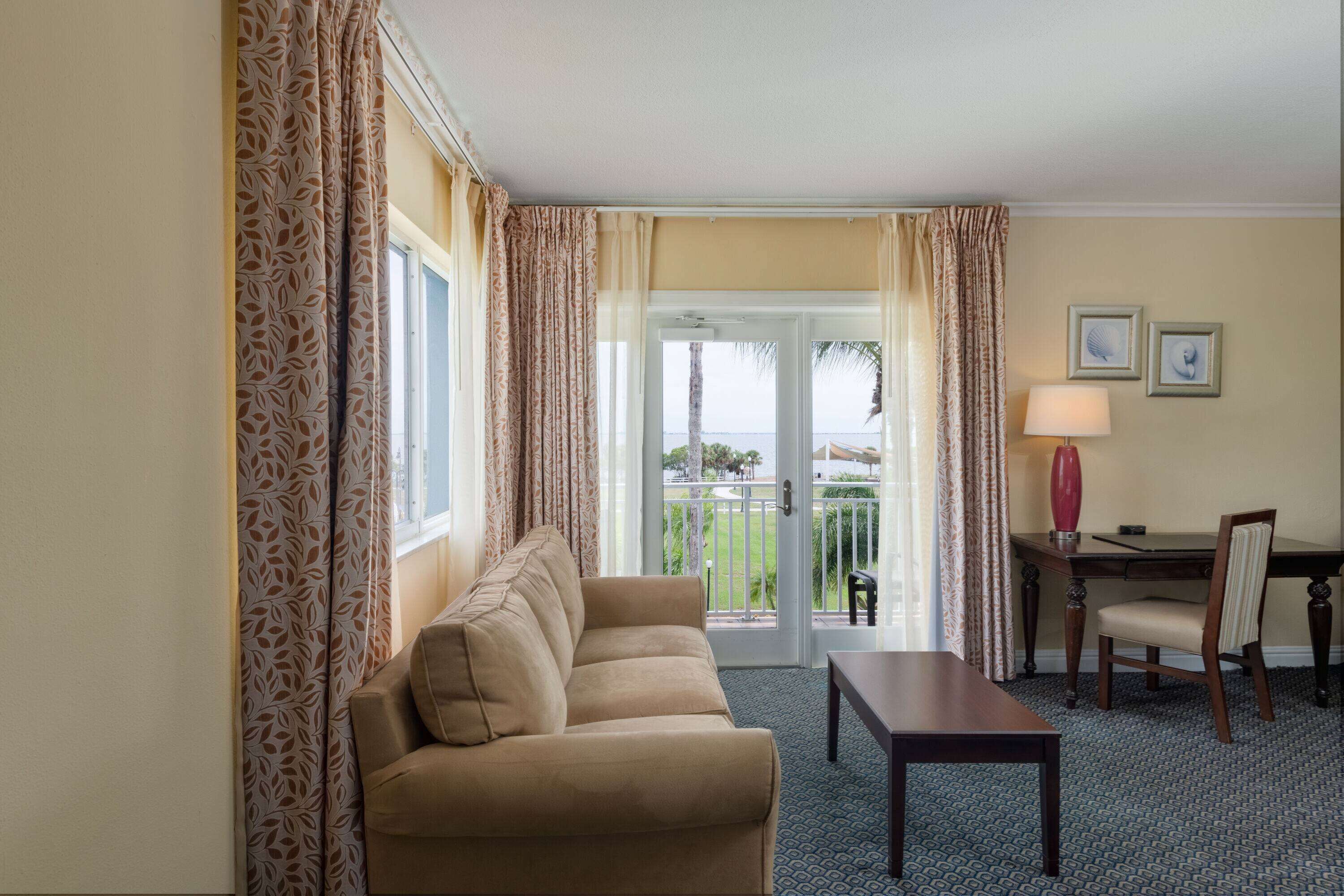 Hotelkamer met een bank, een eettafel, een stoel en uitzicht op het omliggende landschap door een glazen deur.
