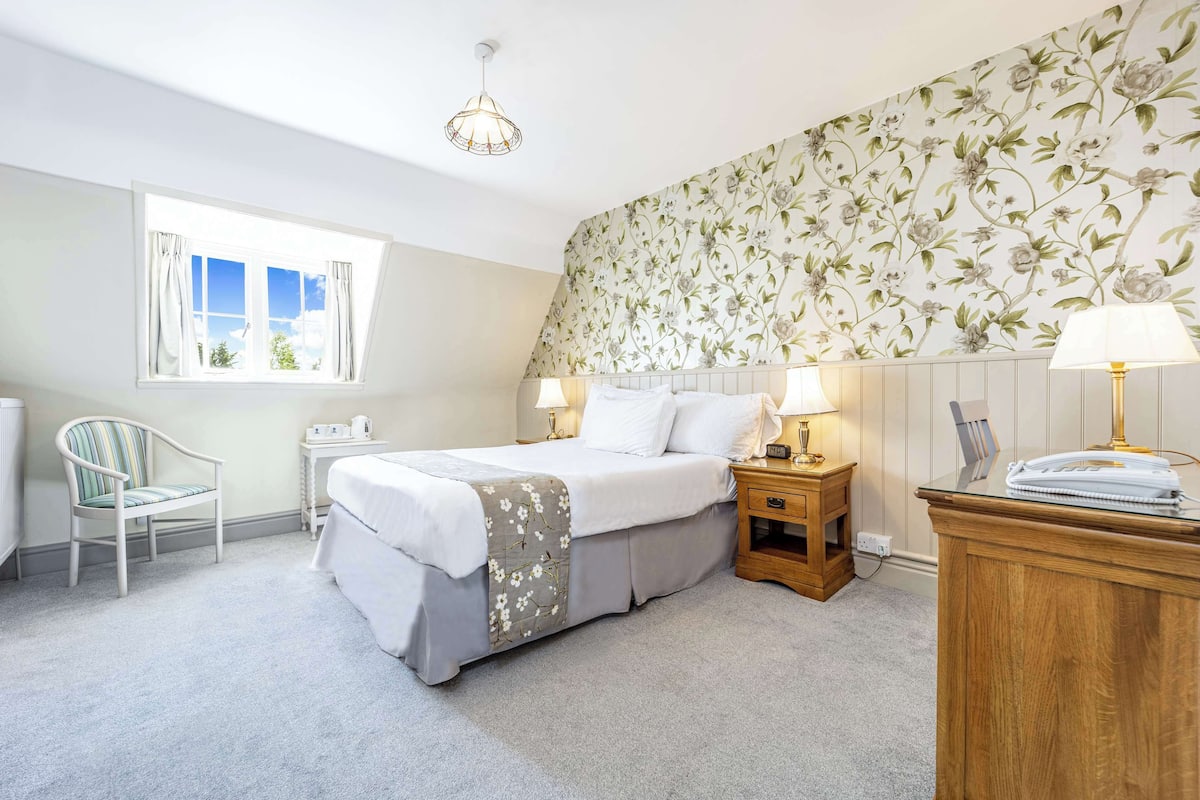 Een slaapkamer met een bed, nachtkastjes, een stoel, een raam en een wand met bloemenbehang.