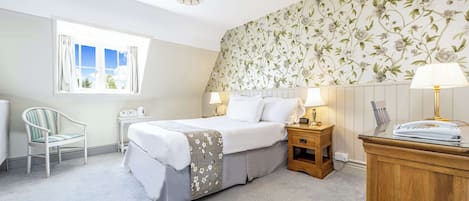 A bedroom with a bed, bedside tables, a chair, a window, and a wall with floral wallpaper.