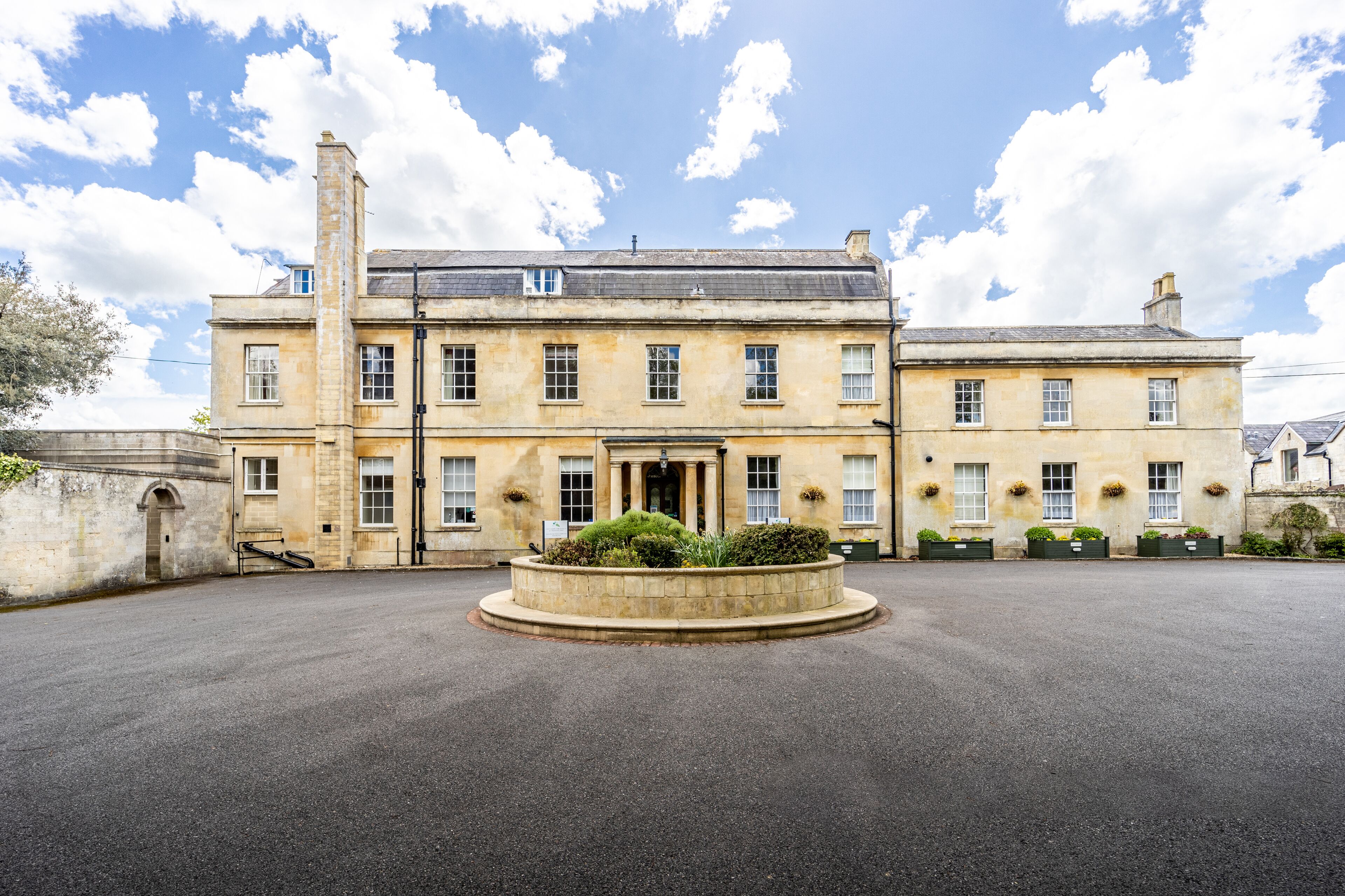 A large, historic building with a central entrance, multiple windows, and a circular driveway.