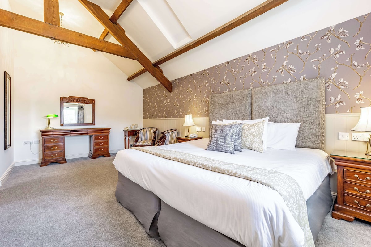 Een slaapkamer met een groot bed, een houten hoofdbord en een bureau met spiegel.