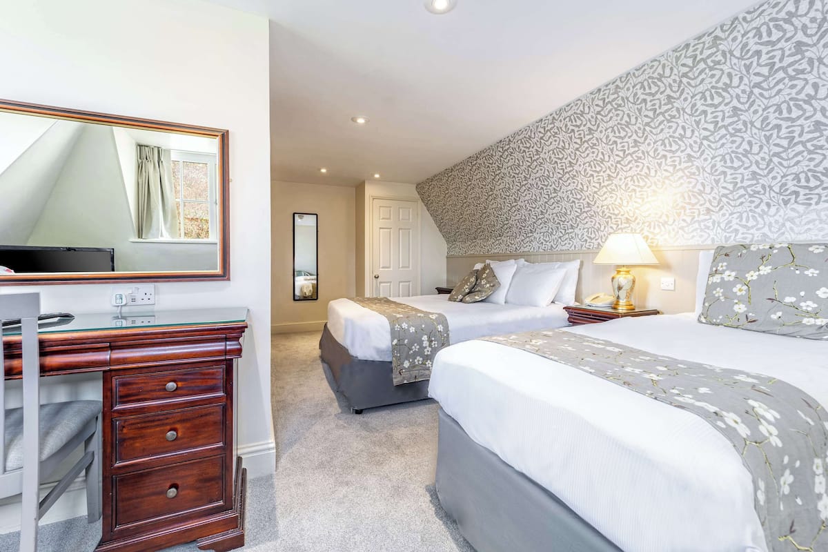 Een hotelkamer met twee bedden, een bureau, een spiegel en een behang met patroon.