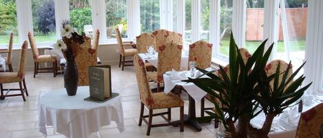 A dining area with multiple tables and chairs, large windows, and a view of the outdoors.