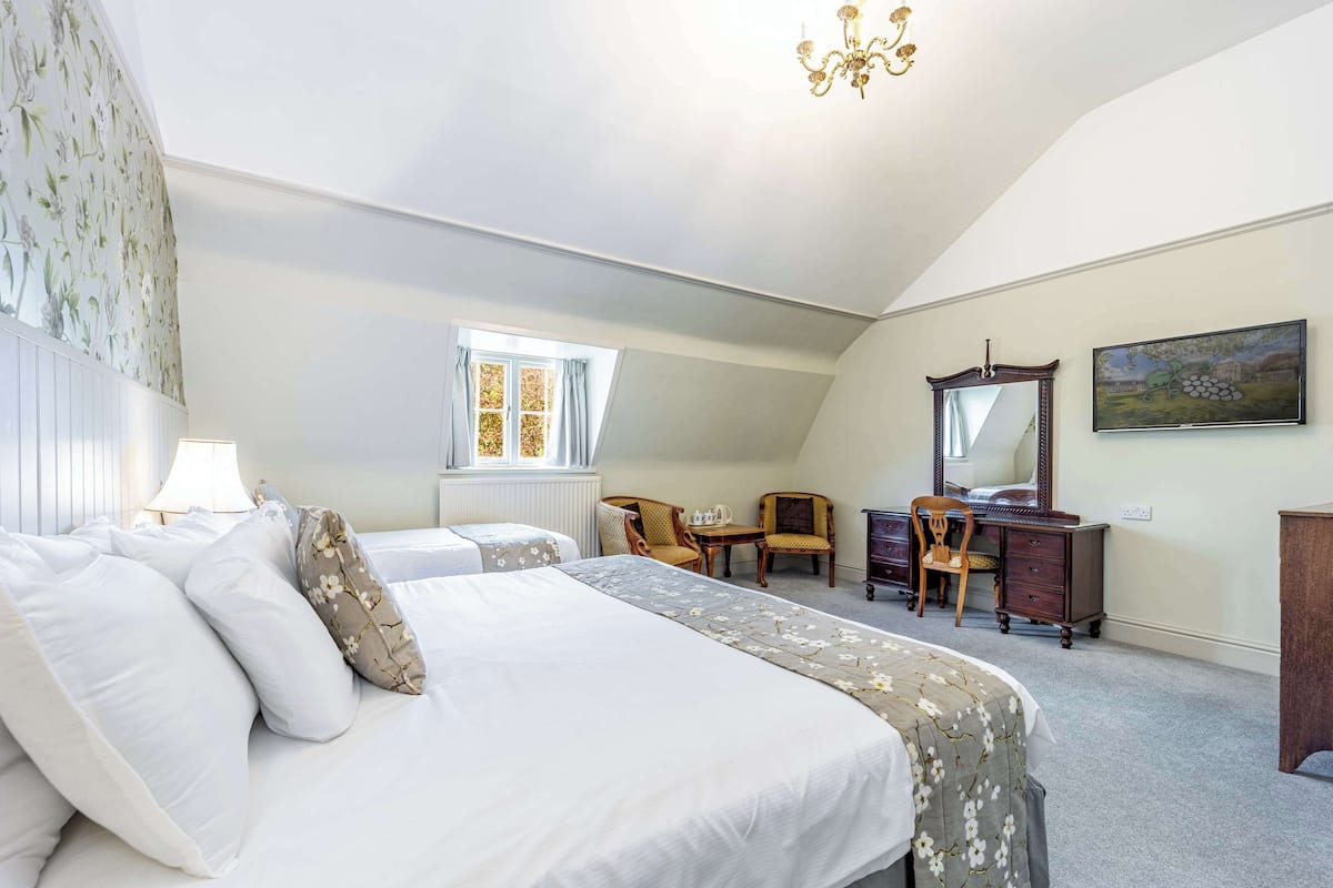 Een slaapkamer met een groot bed, twee stoelen, een kleine tafel, een dressoir en een spiegel.