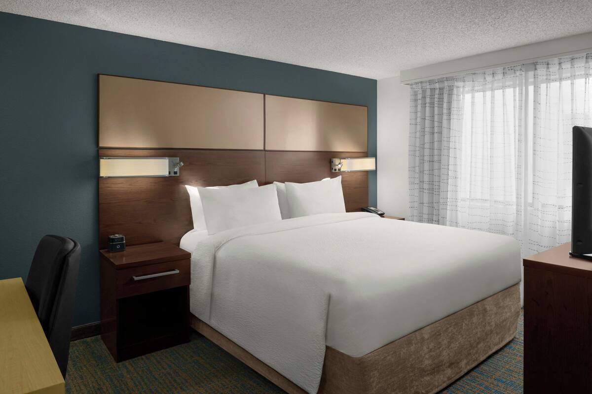 A hotel room with a large bed, a bedside table, a desk, and a television.