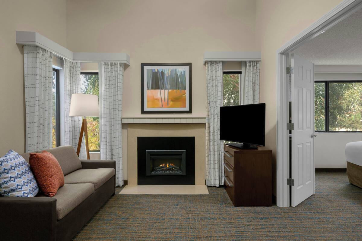 A hotel room with a fireplace, a sofa, a television, and a bed.