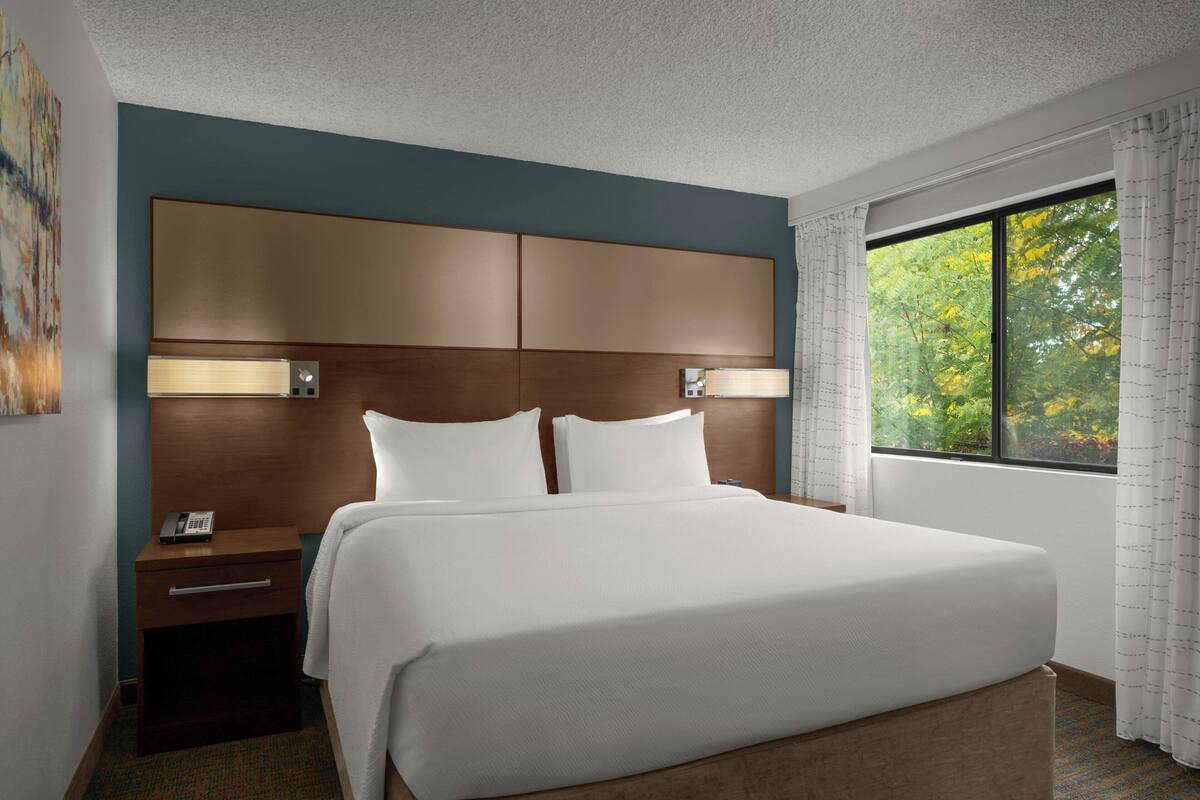 A hotel room with a large bed, a nightstand, a bedside table, and a window with curtains.