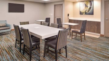 A conference room with a large table, six chairs, a TV, a phone, and a door.