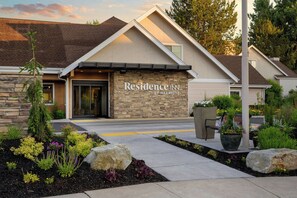 A modern hotel entrance with a stone facade, a covered patio area, and landscaped gardens.