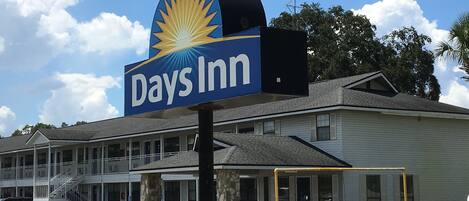 Señal de Days Inn con un logo de rayos de sol, un edificio de dos pisos con entrada cubierta y un estacionamiento.
