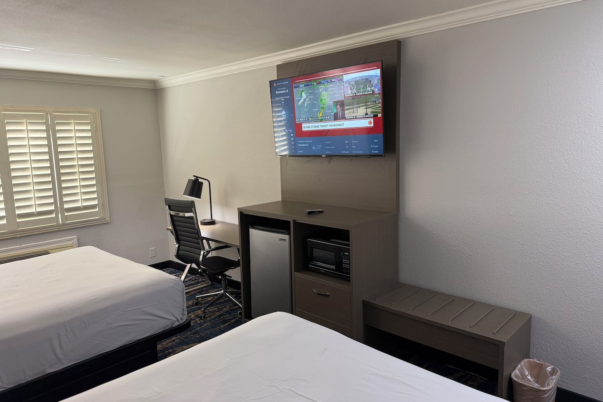 A hotel room with two beds, a desk with a computer, a TV mounted on the wall, and a trash bin.